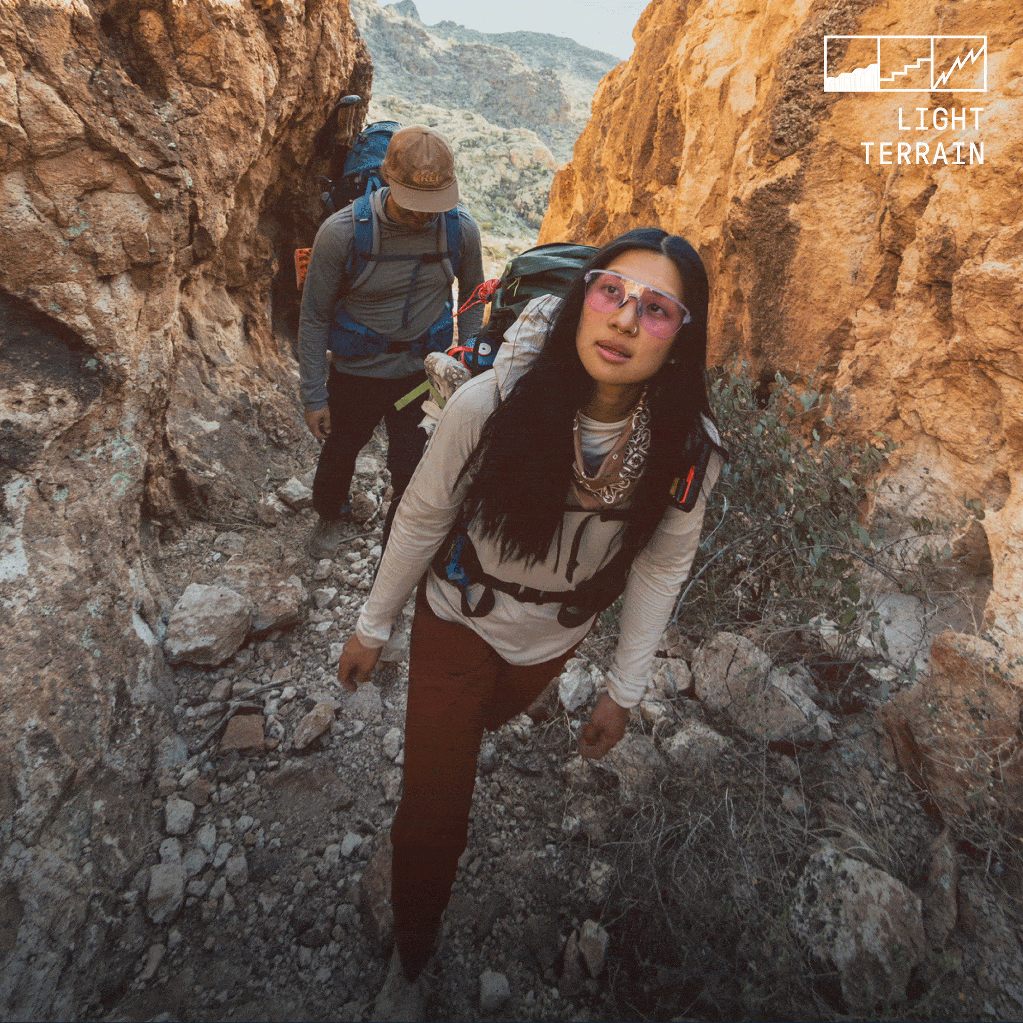 Two people hike through a path surrounded by large rocks.