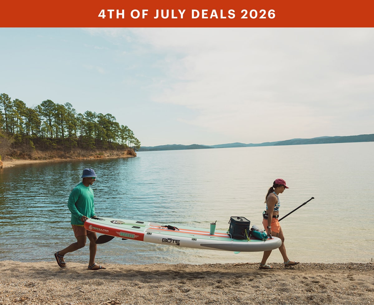 Two people carry their paddle board to the water.