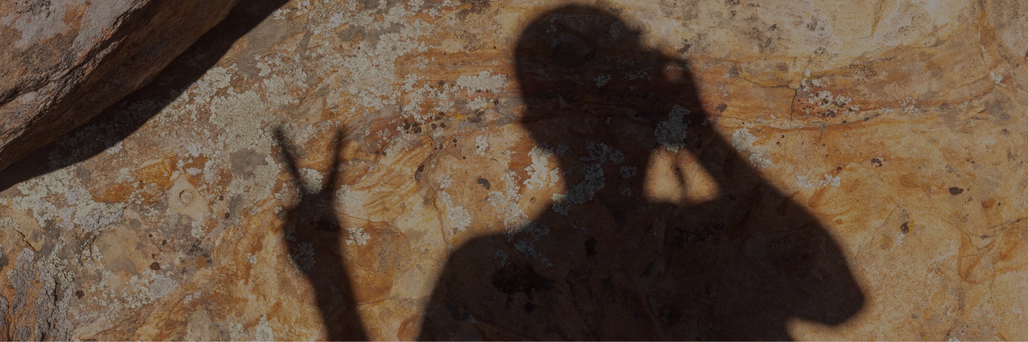 A shadow of a person holding a peace sign against a red rock face.