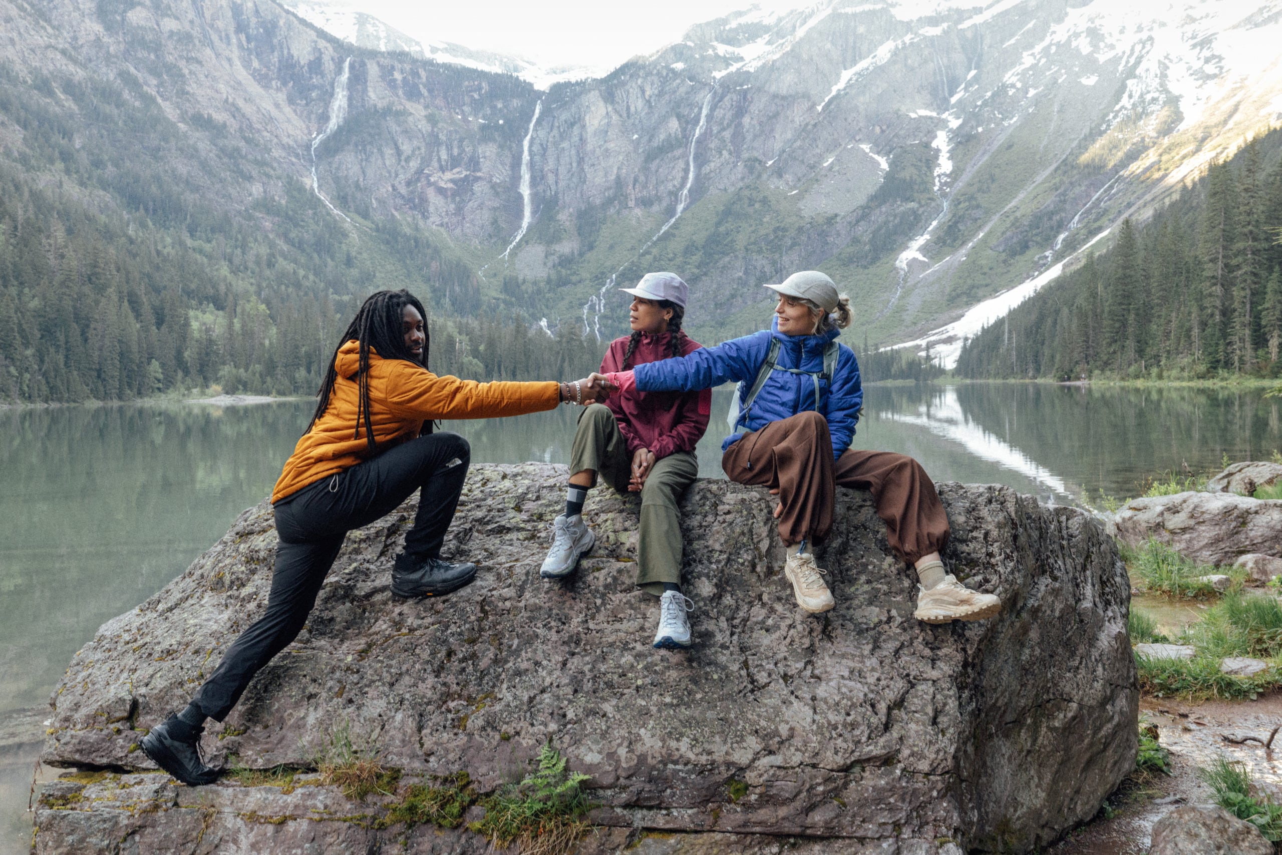 A hiker wearing hiking boots gets help onto a rock where two others rest