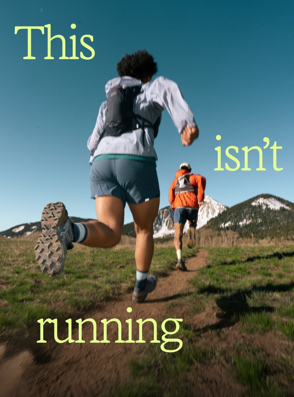 Two people run through a dirt trail towards large mountains. Text reads: ‘This isn’t trail running.’
