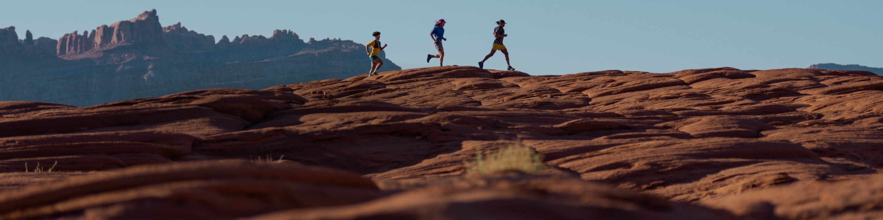 Three people running together over a large rock.