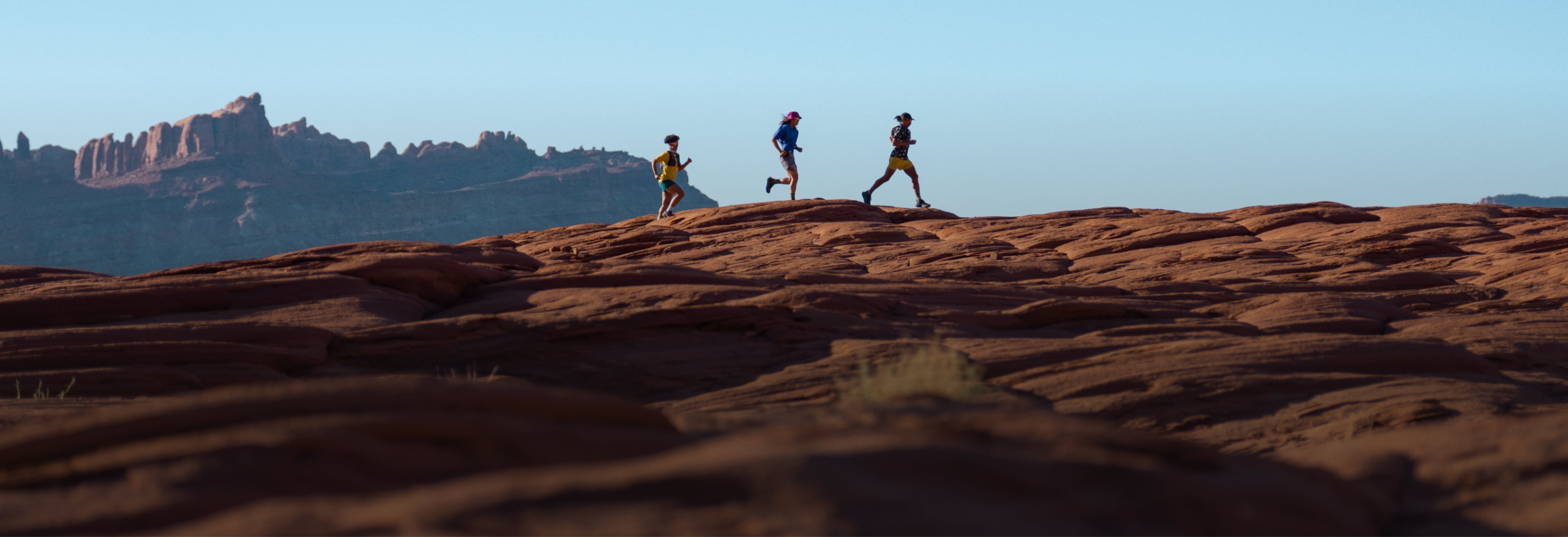 Three people running together over a large rock.