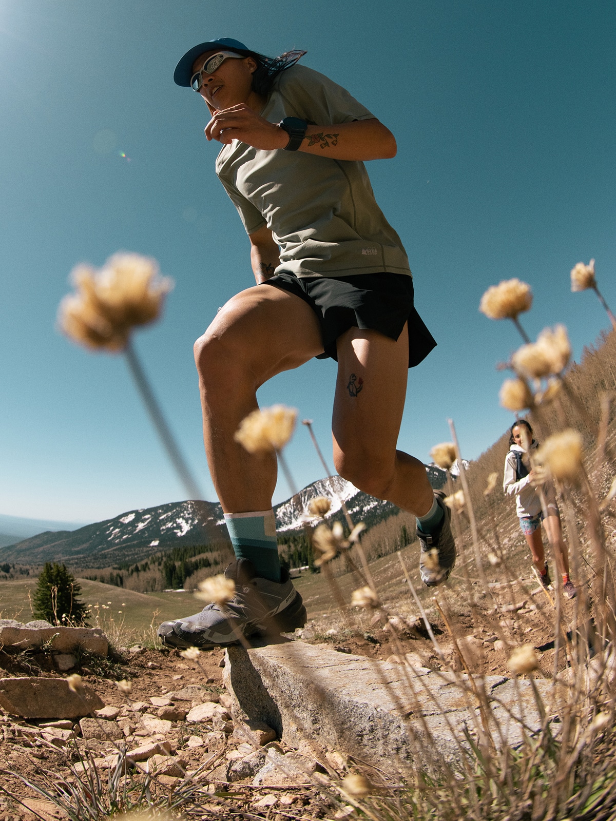 An up close shot of flowers blowing in the wind with two people running in the background.
