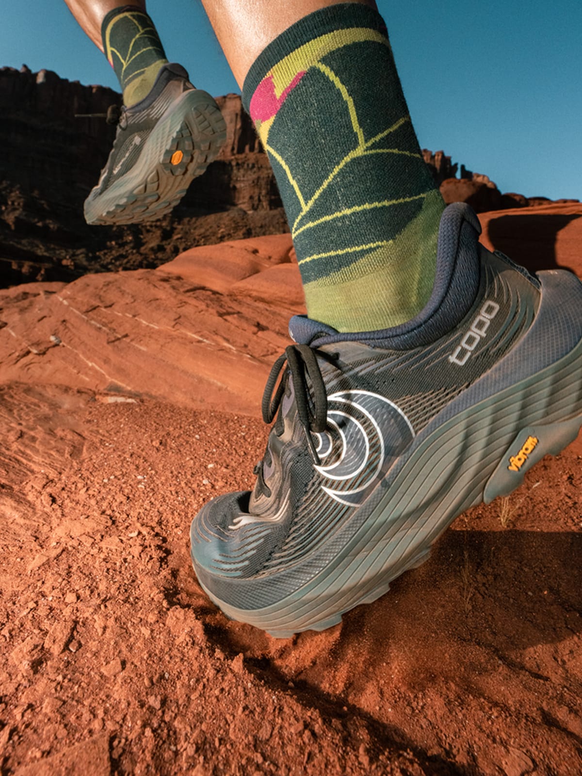 A person runs through a dirt trail in their Topo Athletic running shoes.