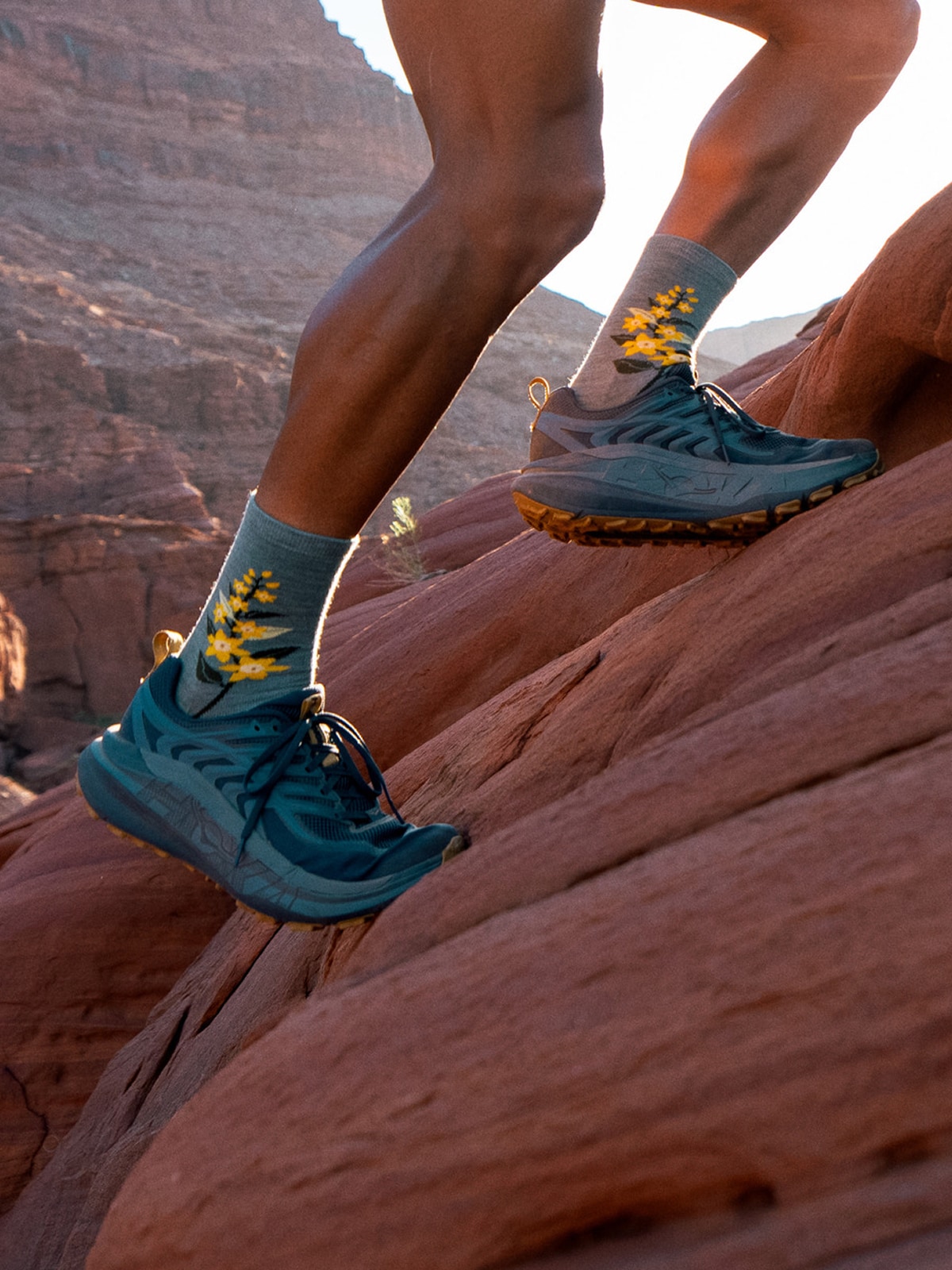 A person runs up a large rock in their HOKA running shoes.