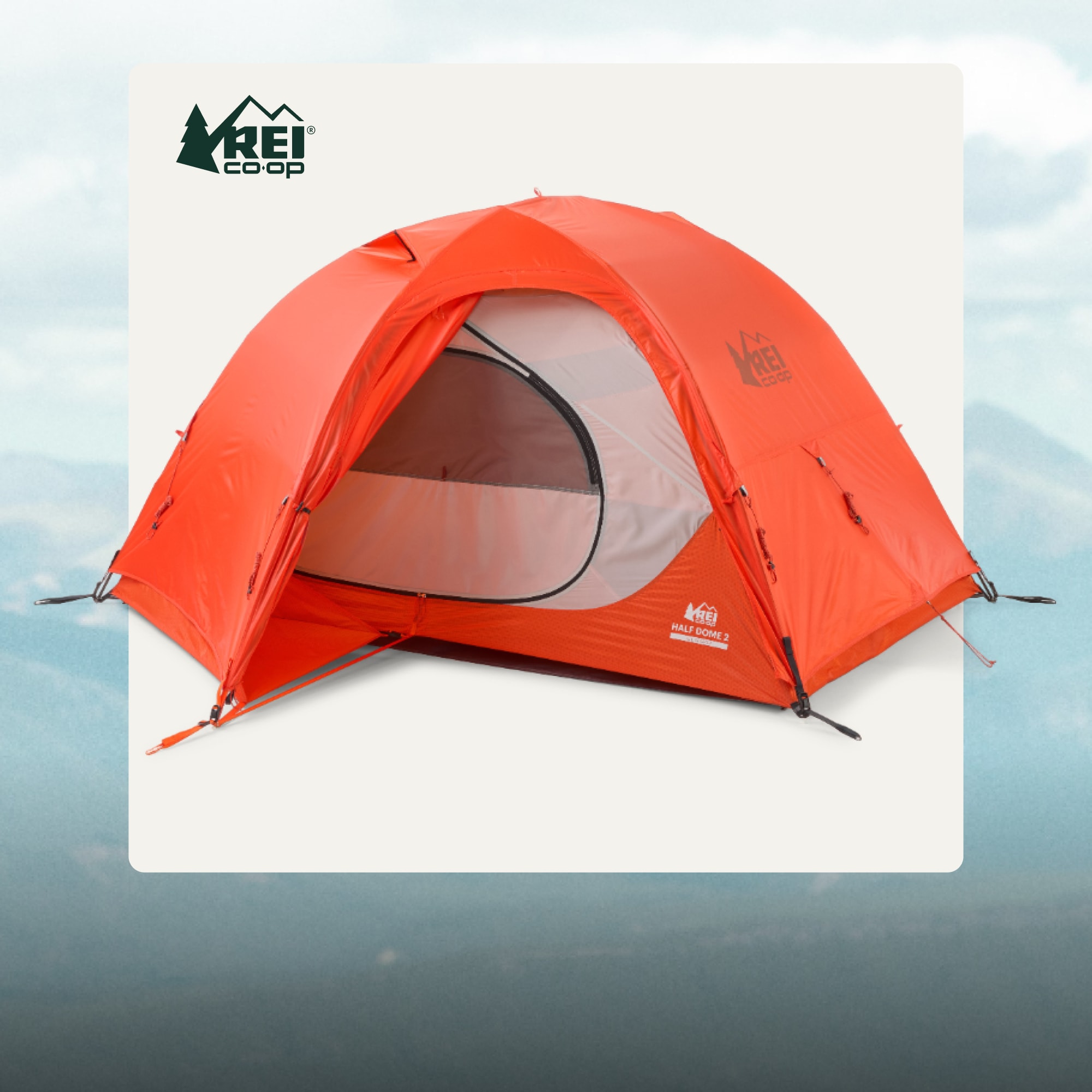 An R E I Co-op Half Dome 2 All-Season Tent on a light colored background over an image of snowy mountains.
