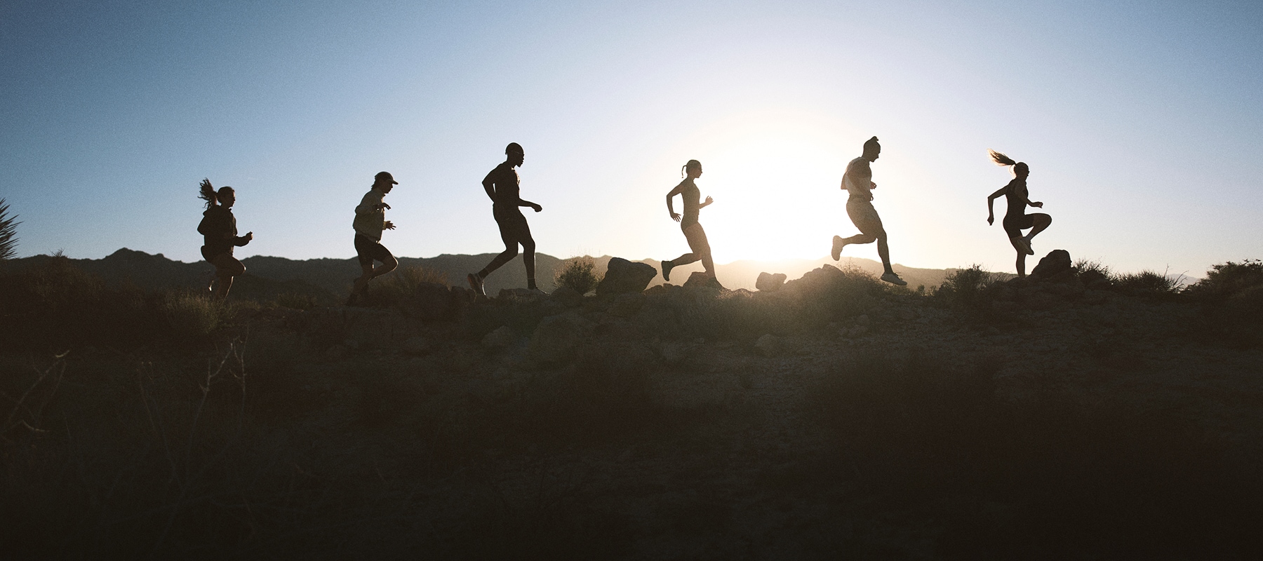 Silhouettes of a group of people running through a rocky trail.