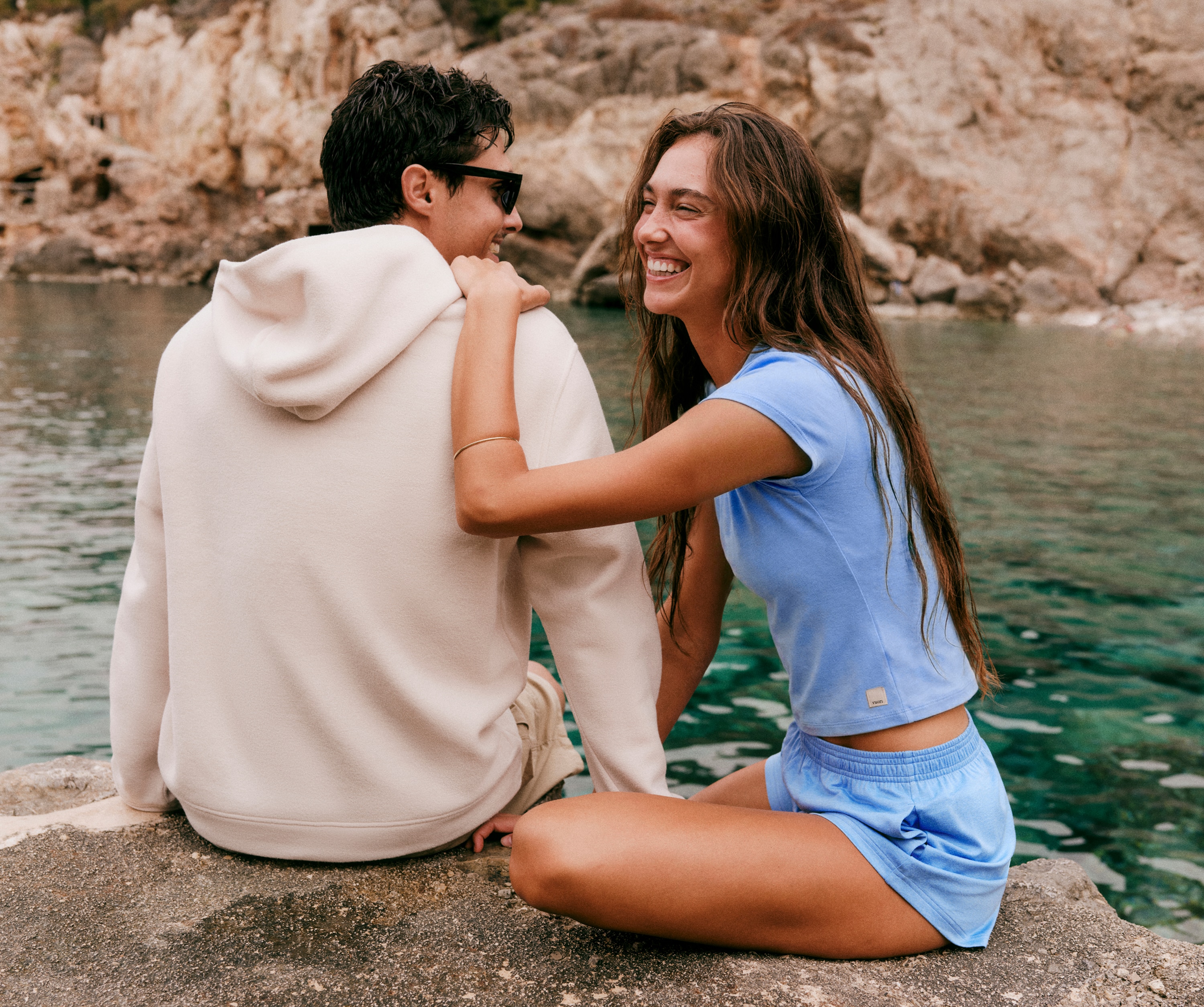 Two people sitting near a body of water in their Vuori clothing.