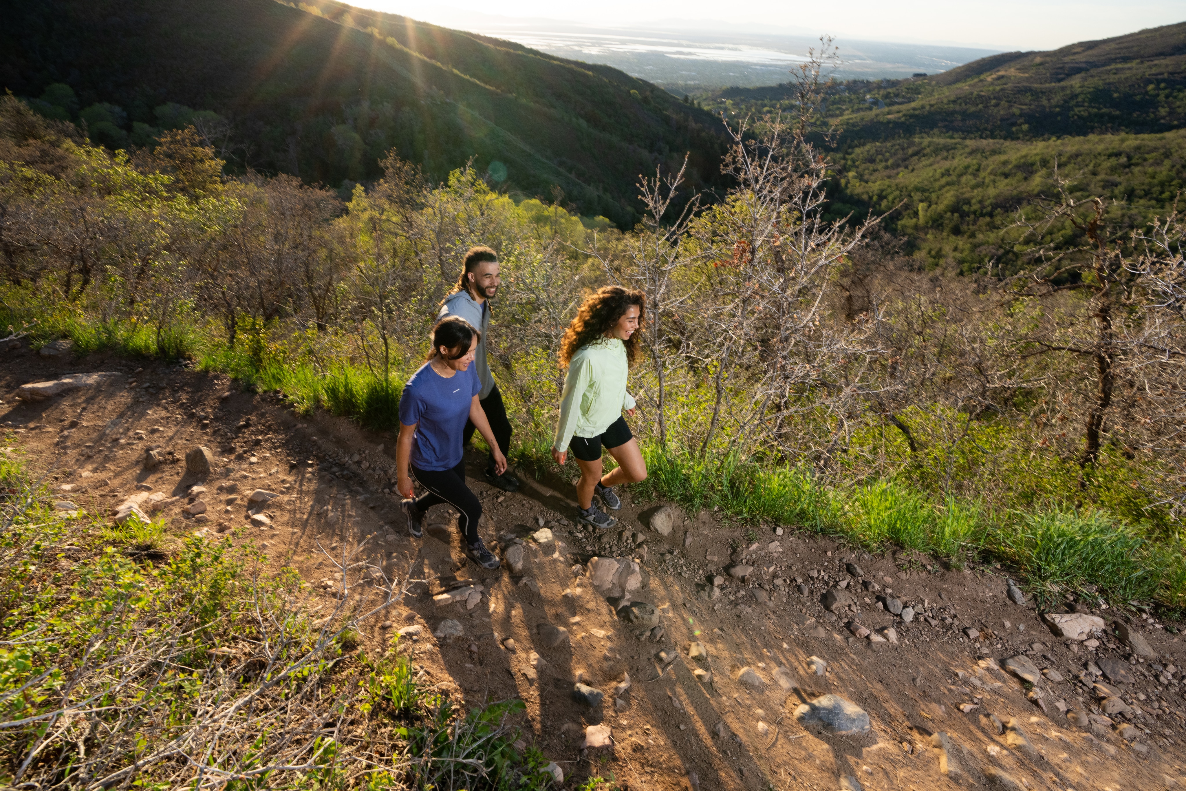 A group of people hike through a rocky path together with a view of tree-covered mountains in the background.