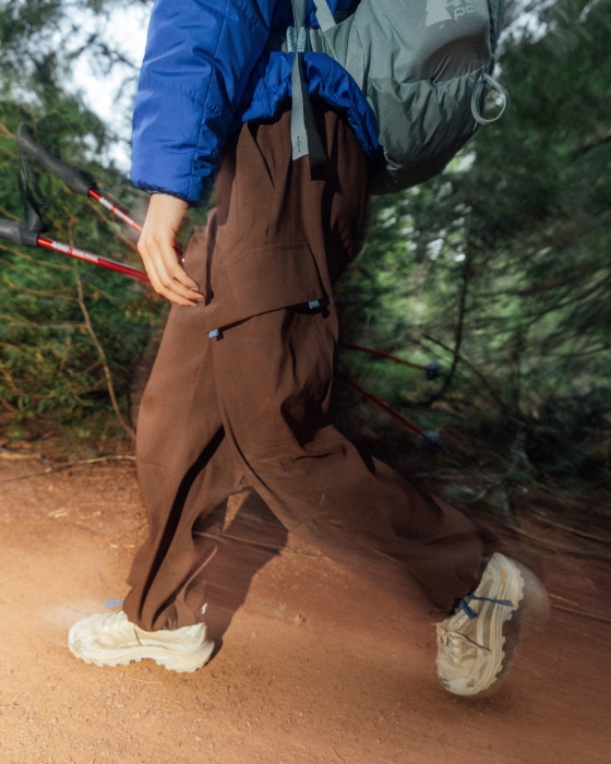 A photo from the waist down of someone hiking through a dirt trail with a backpack on and trekking poles in one hand.