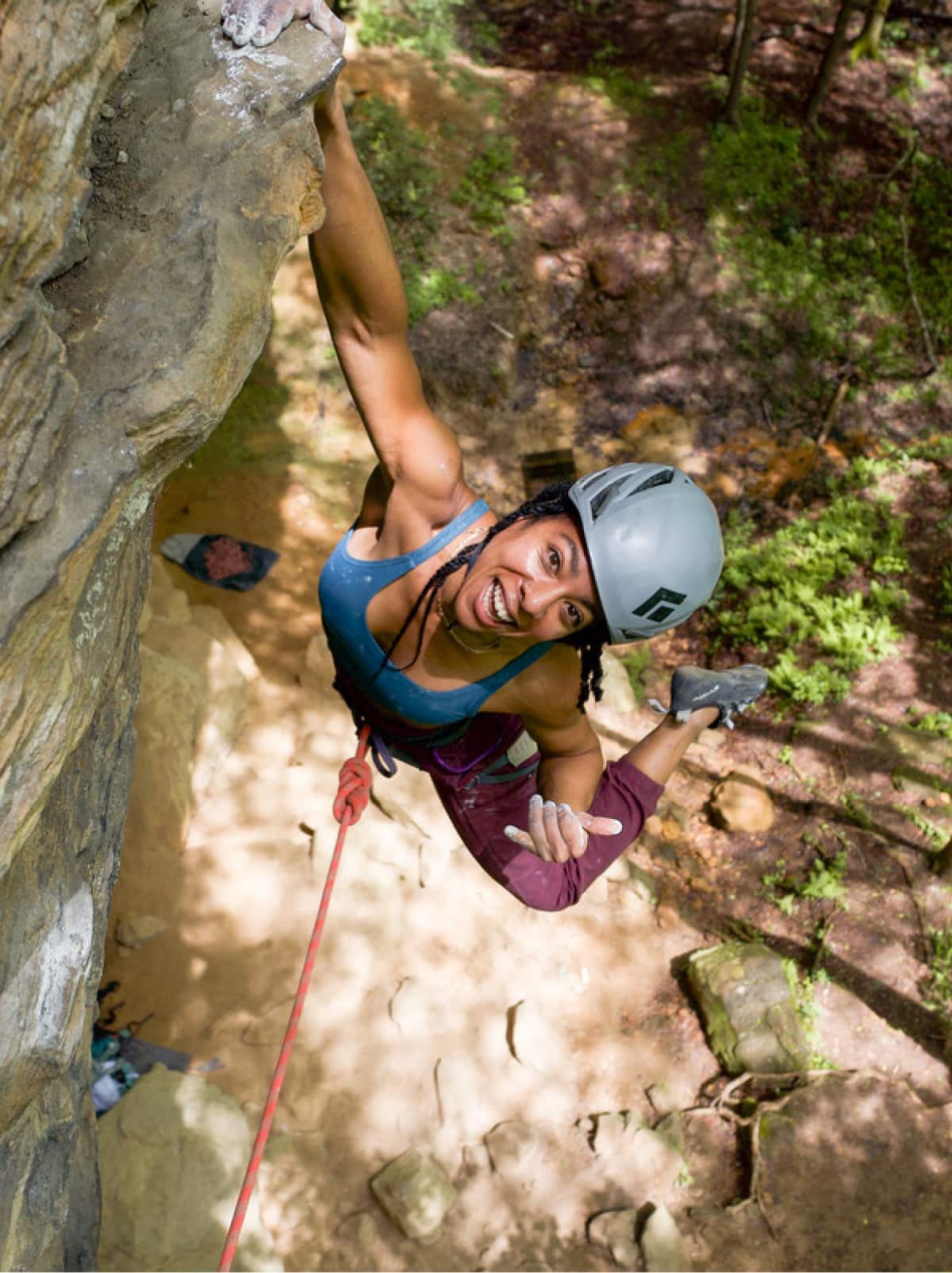 A person smiles for the camera while hanging from the face of a rock.