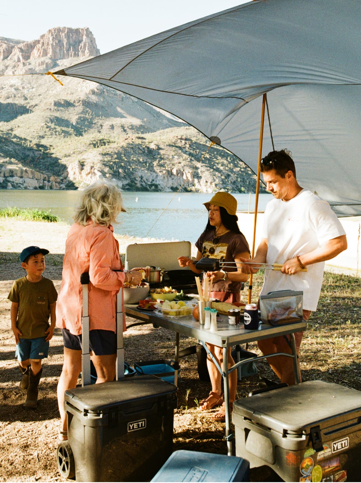 A group of people gather around a table and prepare to cook at their campsite.