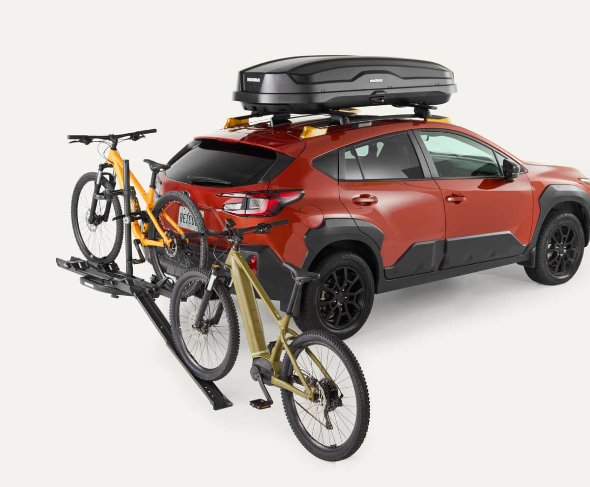 A red car with two bikes on a Yakima bike rack on a light colored background.