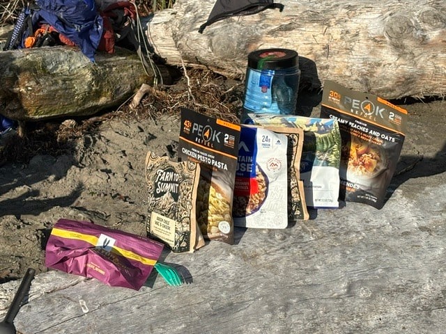 a collection of backpacking meals lined up on a log on the beach