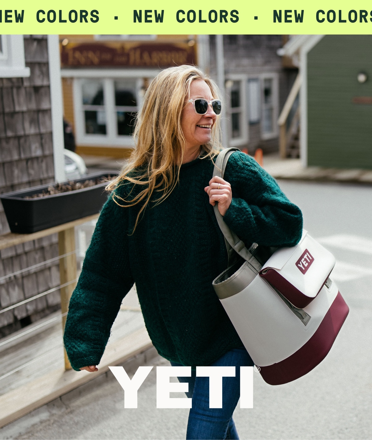 A person walks through the street while carrying a YETI tote bag. Ticker tape reads: ‘New colors.’