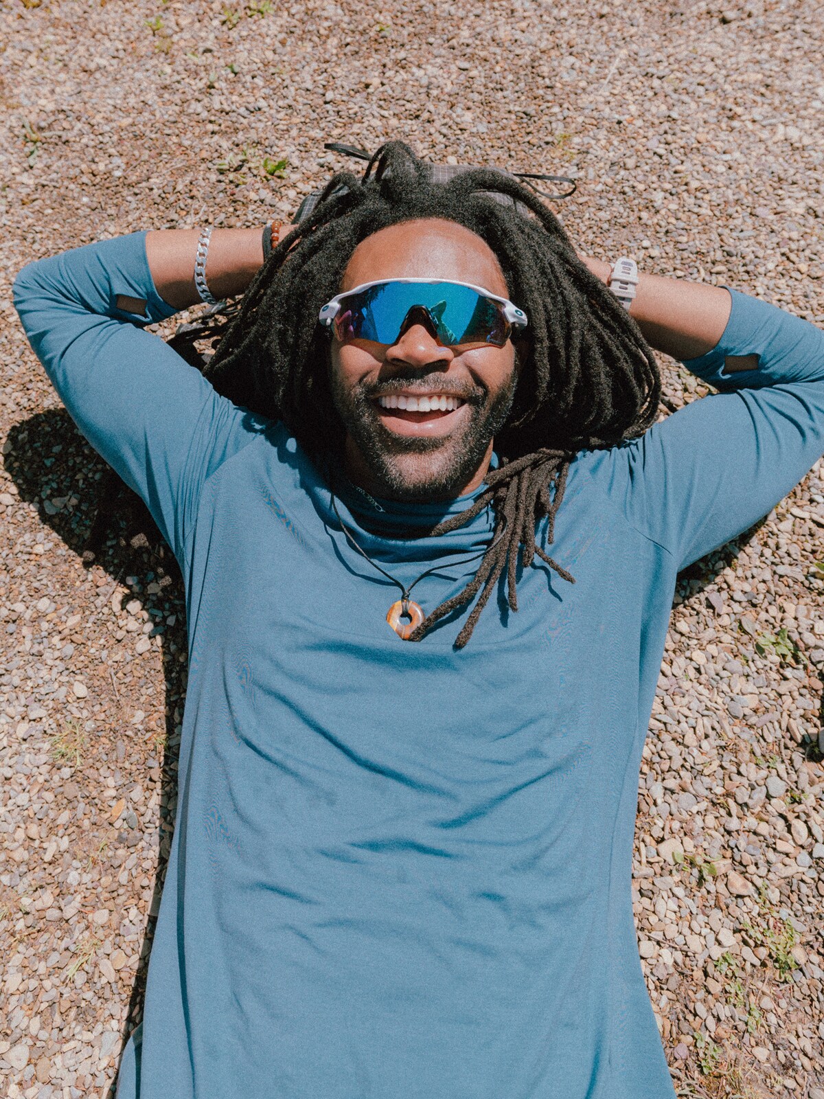 A person smiles for the camera while laying on the ground with their arms behind their head.