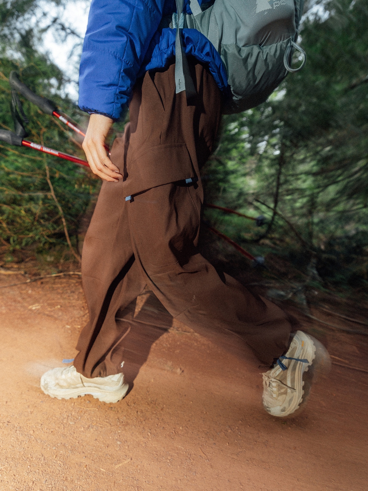 A person hiking through a dirt trail with a backpack on and trekking poles in their hand. 