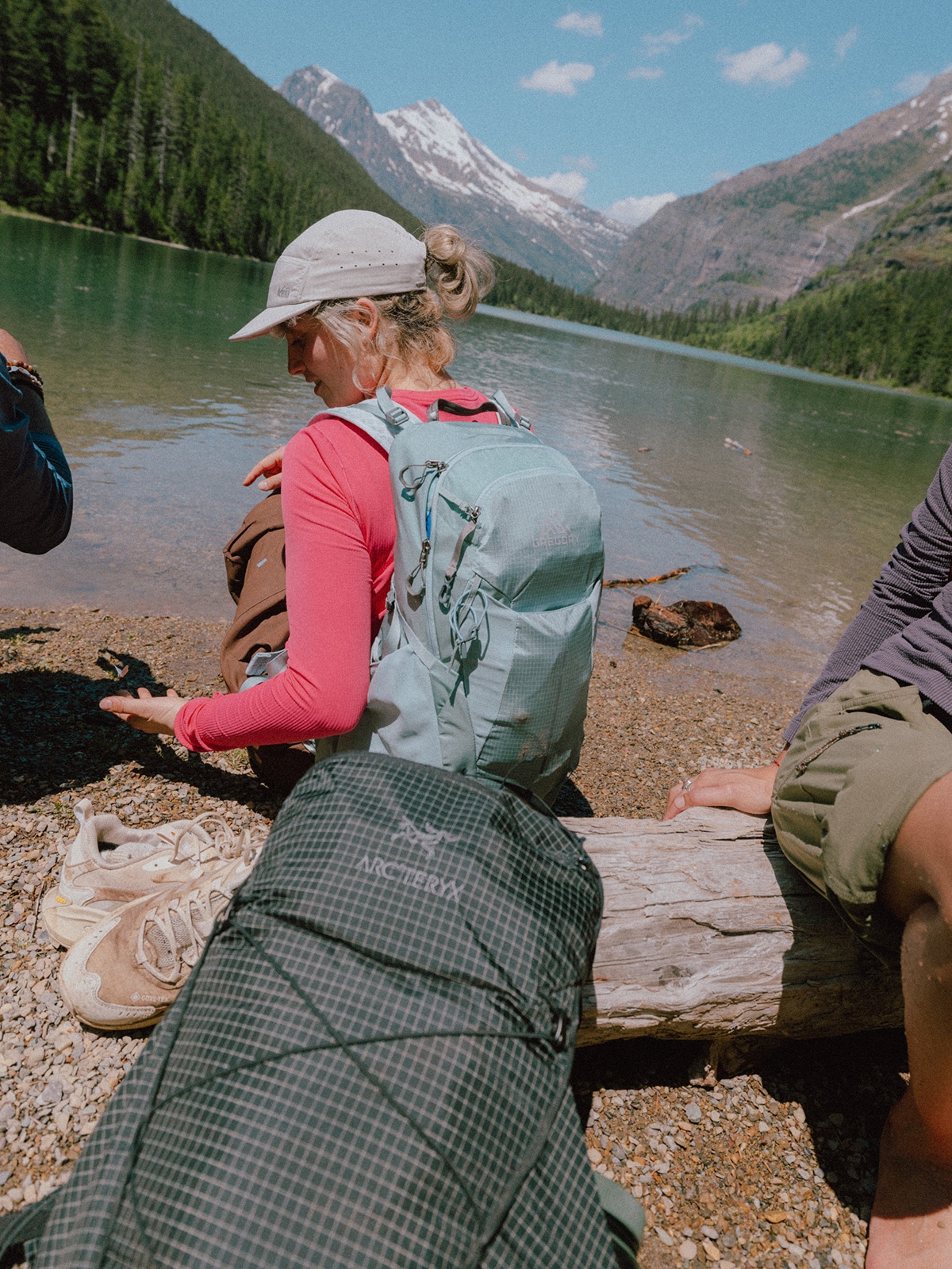 A group of hikers sitting near a lake with a view of mountains in the background.