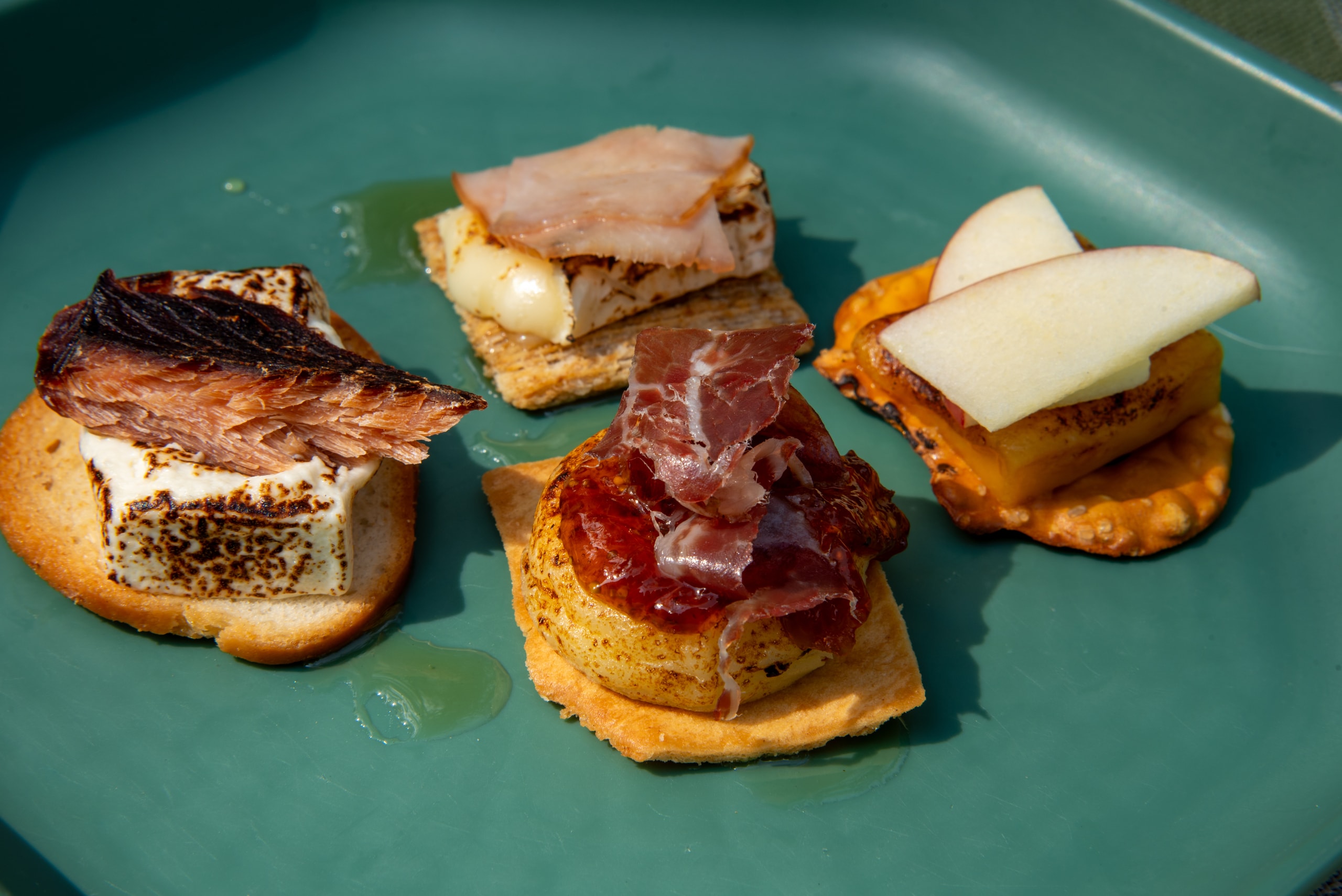 A green plate with four unique takes on s'mores including bacon, apples, cheese and ham.
