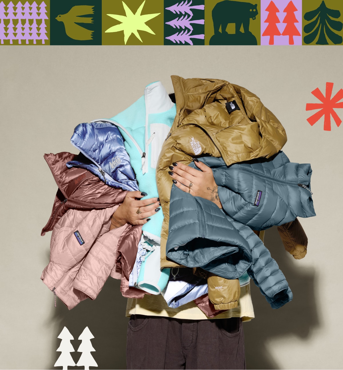 A person holding a variety of winter jackets on a light colored background.