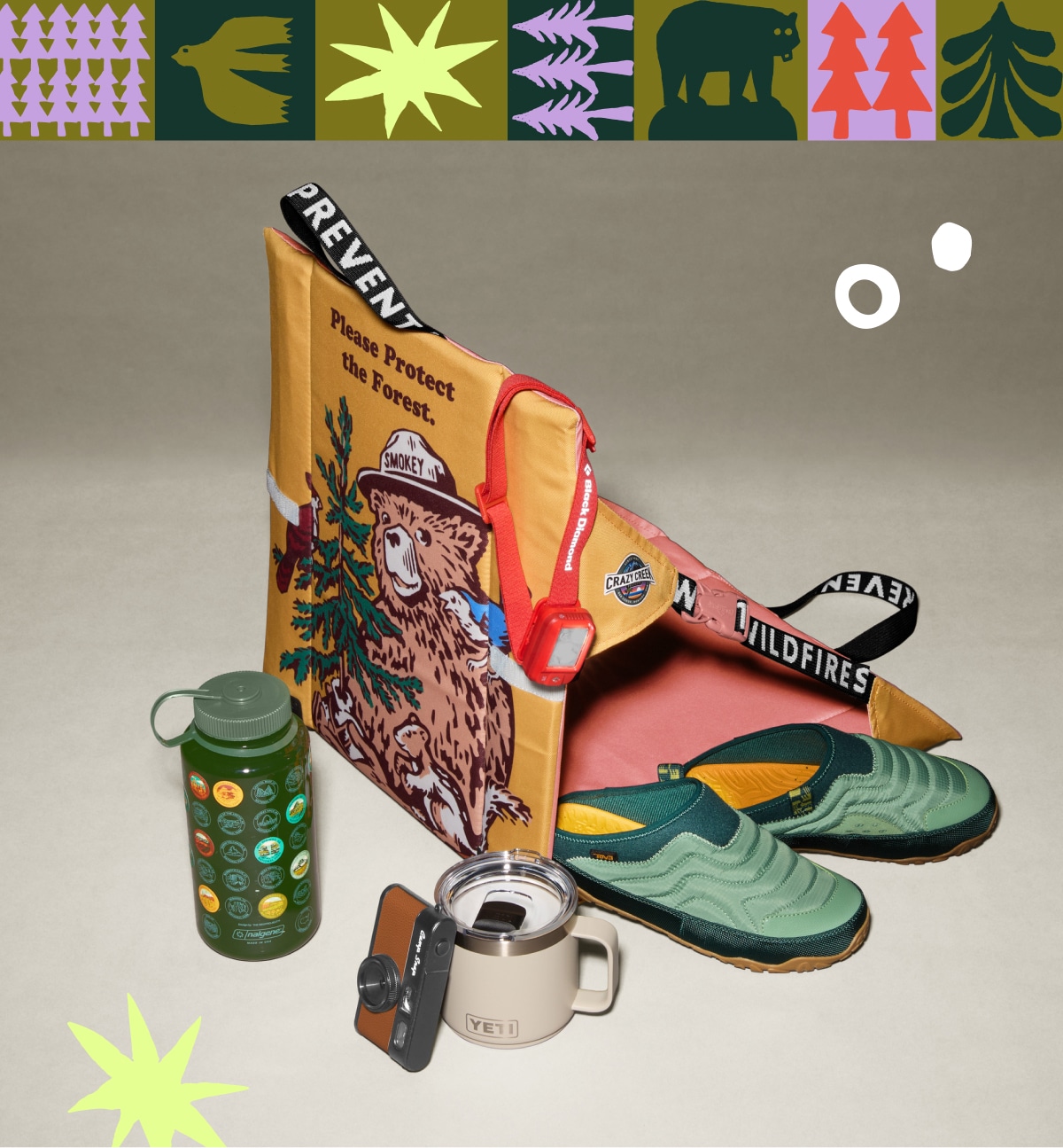Drinkware, a headlamp, a pair of Teva shoes, a Crazy Creek chair and a Camp Snap camera on a light colored background.