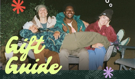 Text reads ‘Gift Guide’ over an image of three people laughing and smiling while camping.