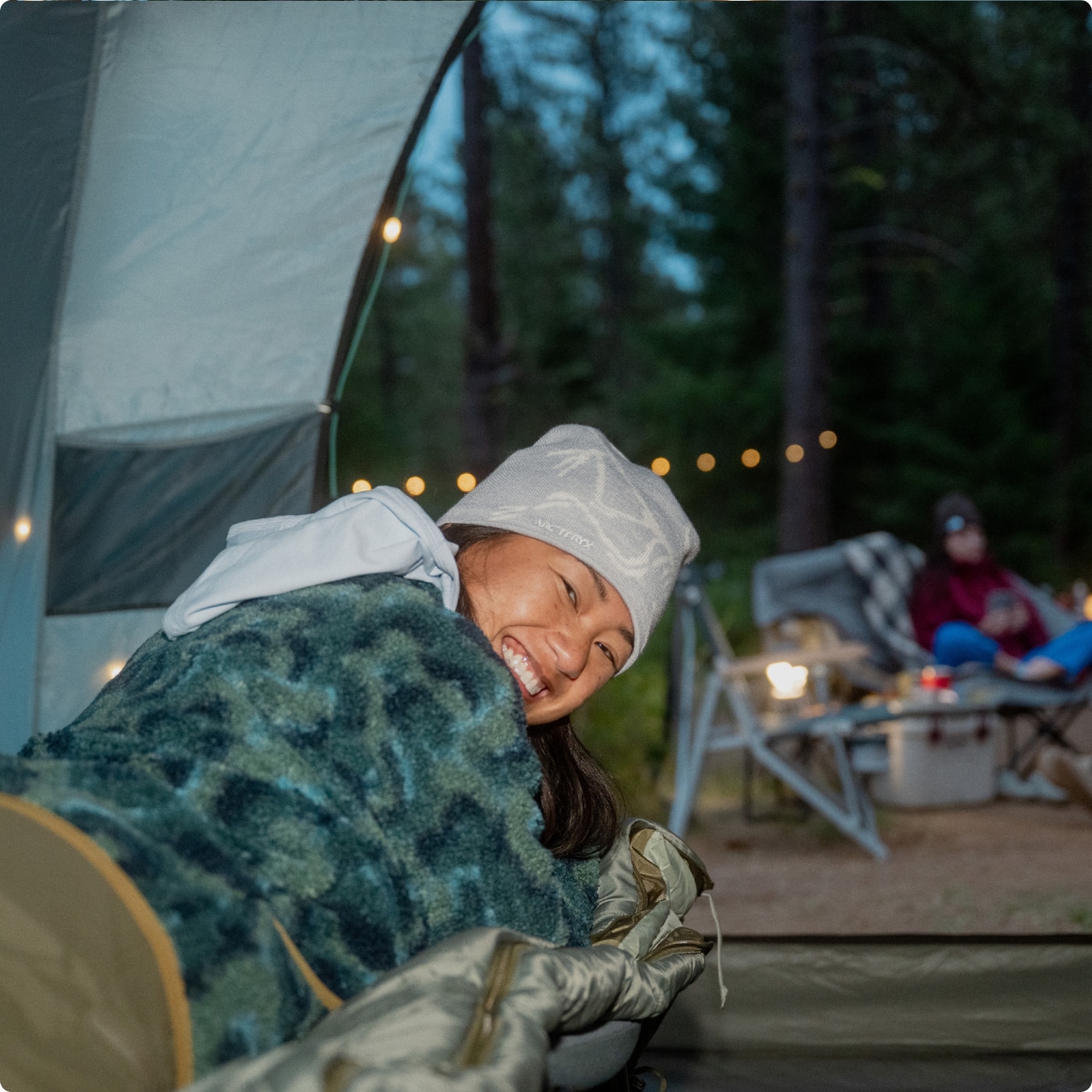 A person smiles for the camera while laying down on a cot inside of a tent.