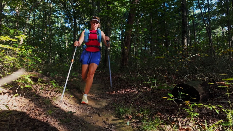A woman fastpacking on a forest trail.