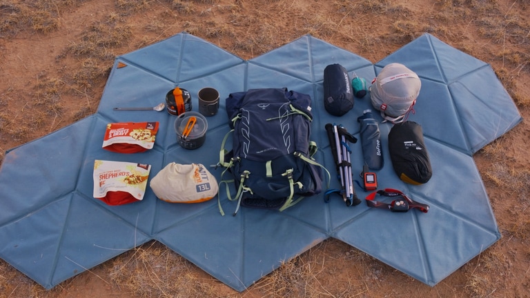 Fastpacking gear layed out on a geometric-shaped mat, including backpacking food, kitchen gear, a backpack, a sleeping bag, trekking poles, a tent, a headlamp, and more.
