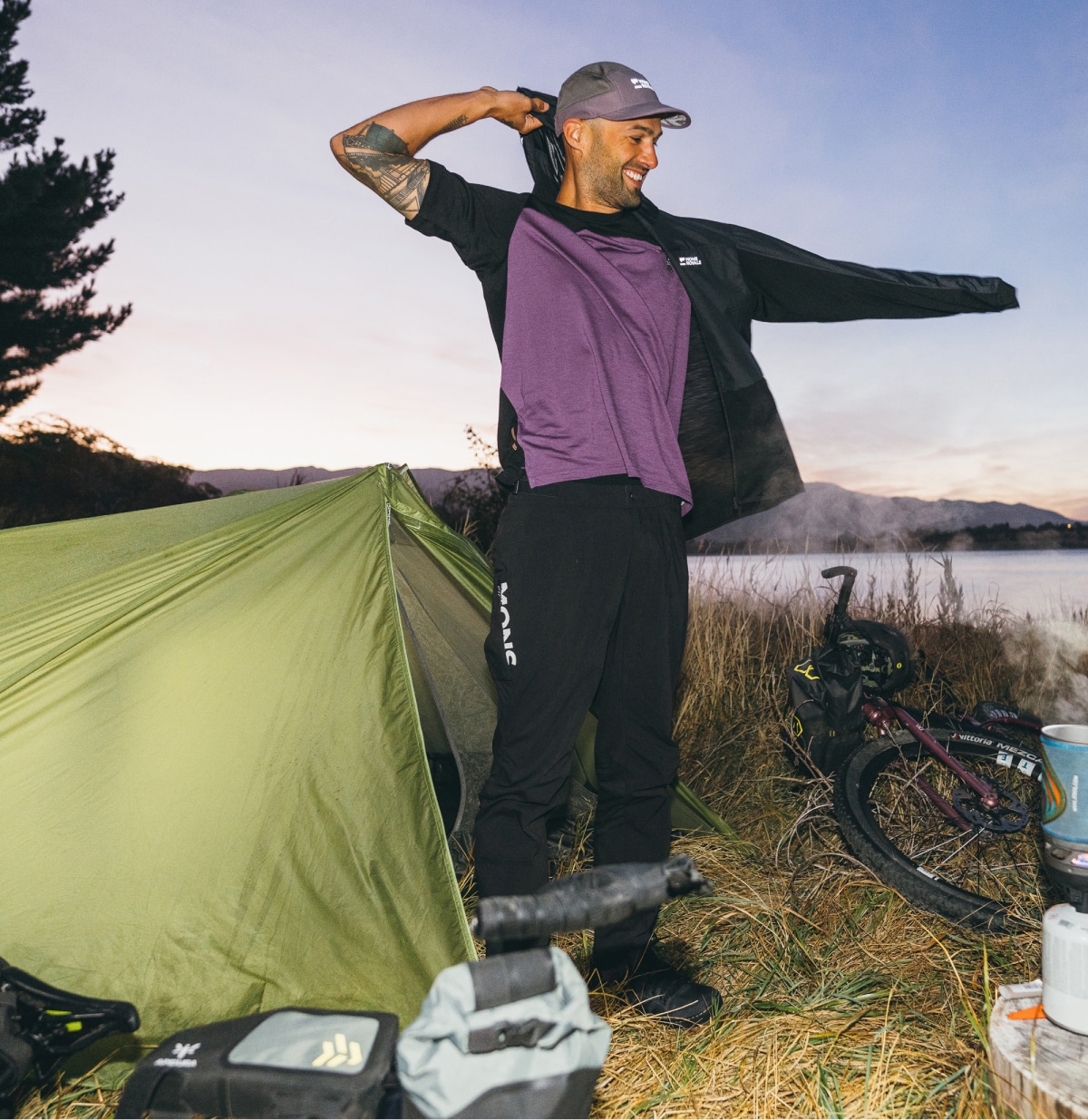 A person puts their jacket on while standing outside of a tent.