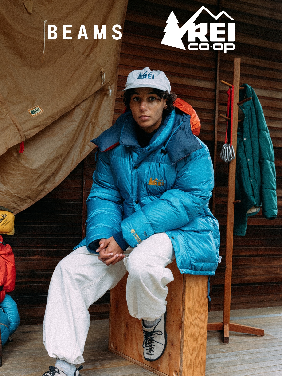 A person sitting down on a wooden box in a blue BEAMS x R E I Co-op Expedition Parka.