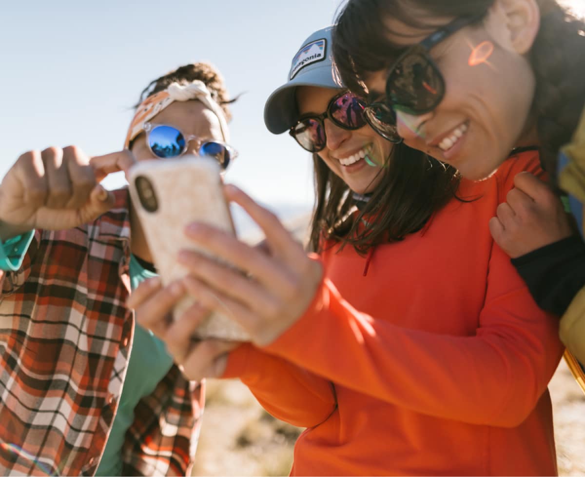 Three people smile while looking at a cellphone.