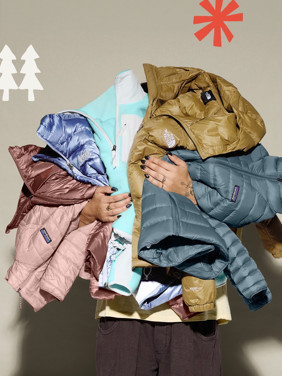 A person holding a variety of jackets on a light colored background.