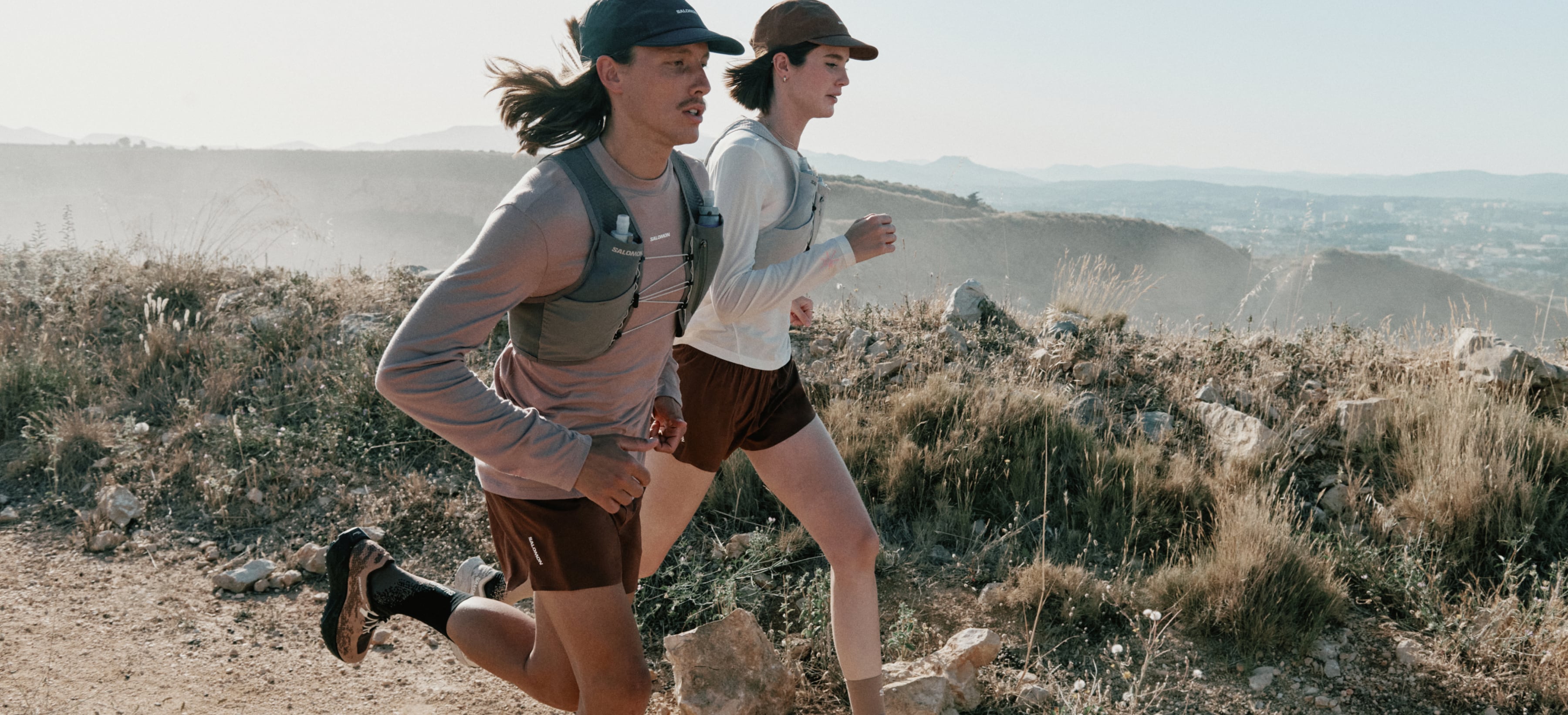 Two people run together through a dirt trail on a sunny day.
