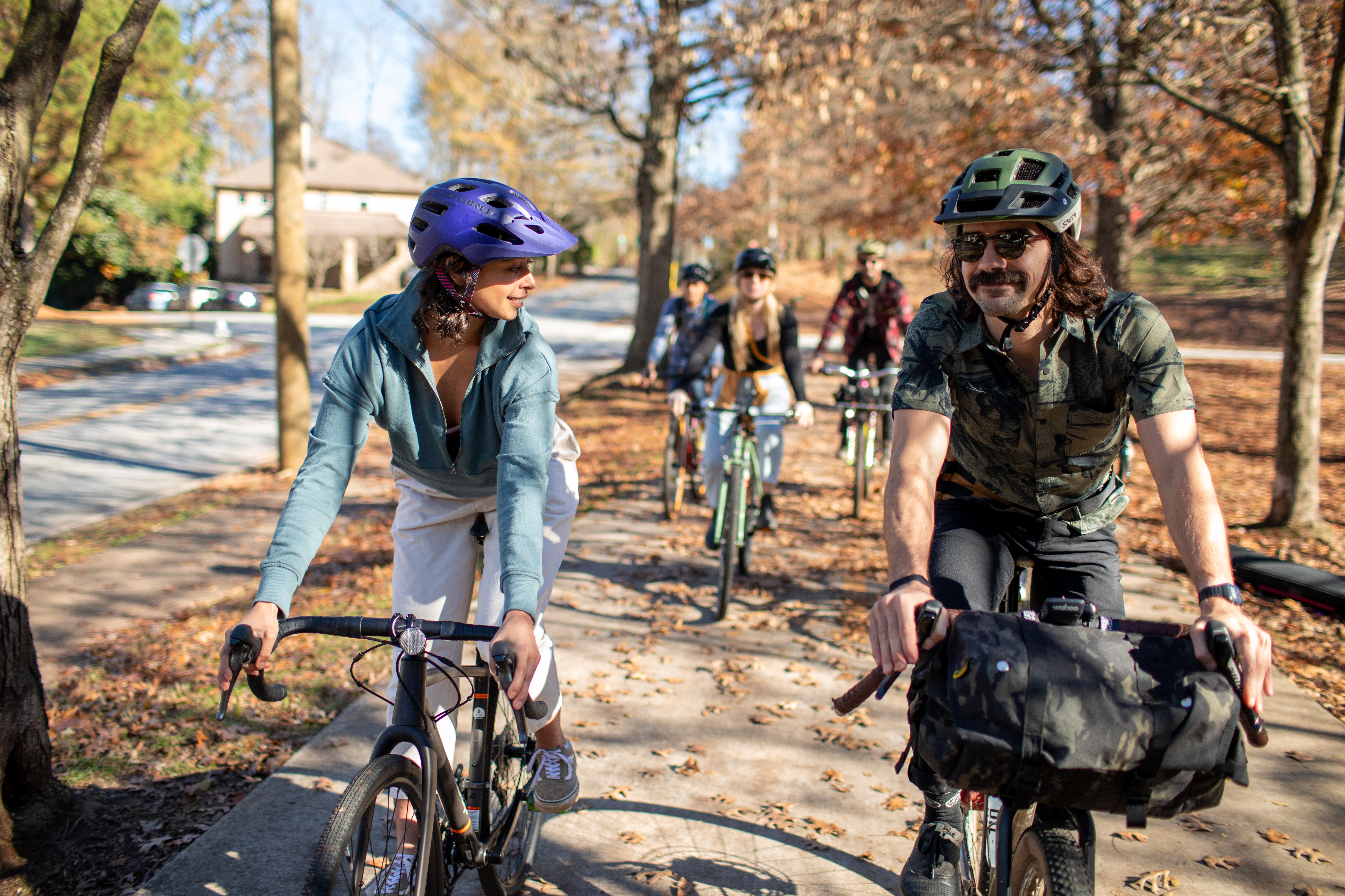 A group of five bike riders ride on a paved trail through trees
