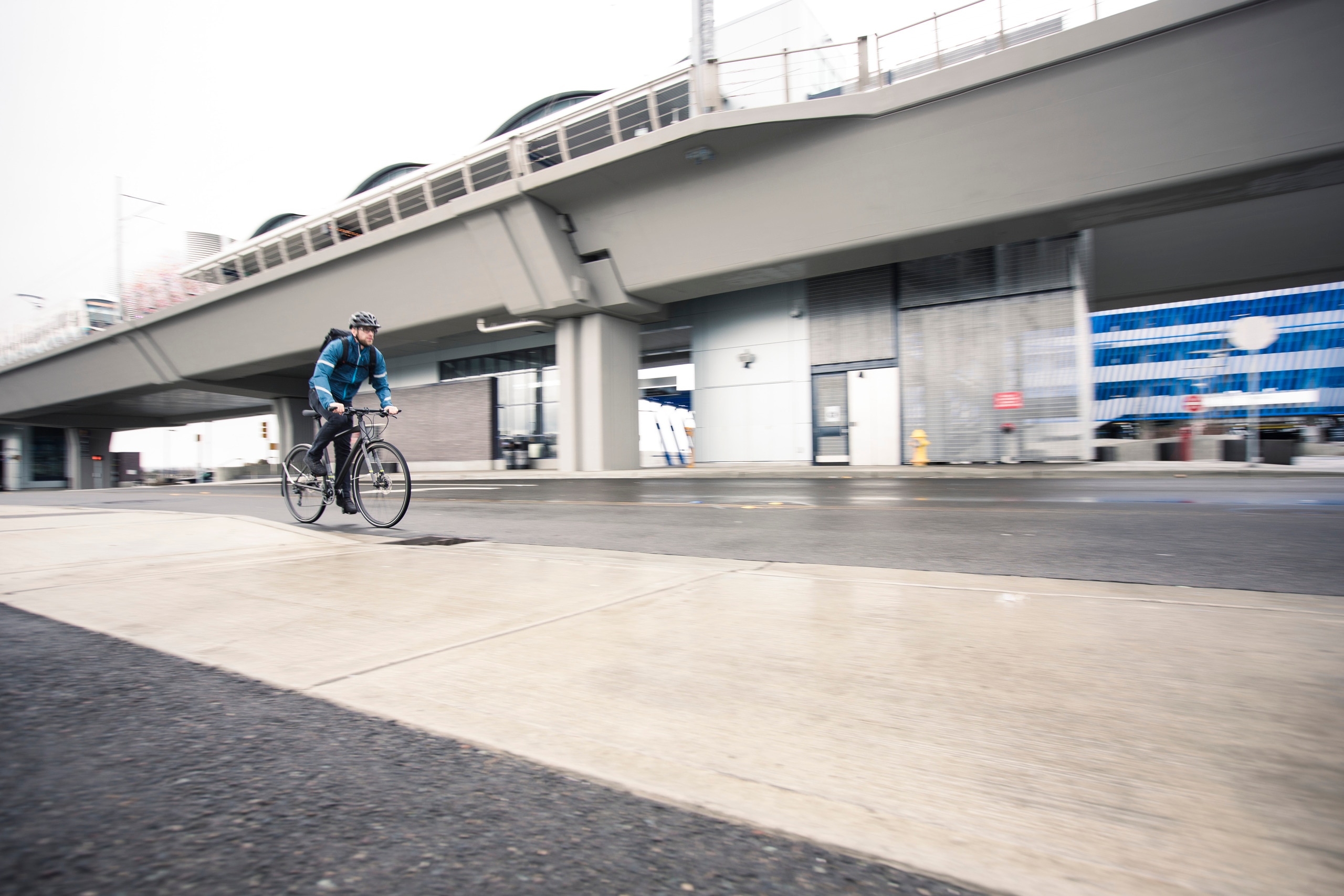 A person wearing a rain jacket bikes on a slick street in an urban setting.