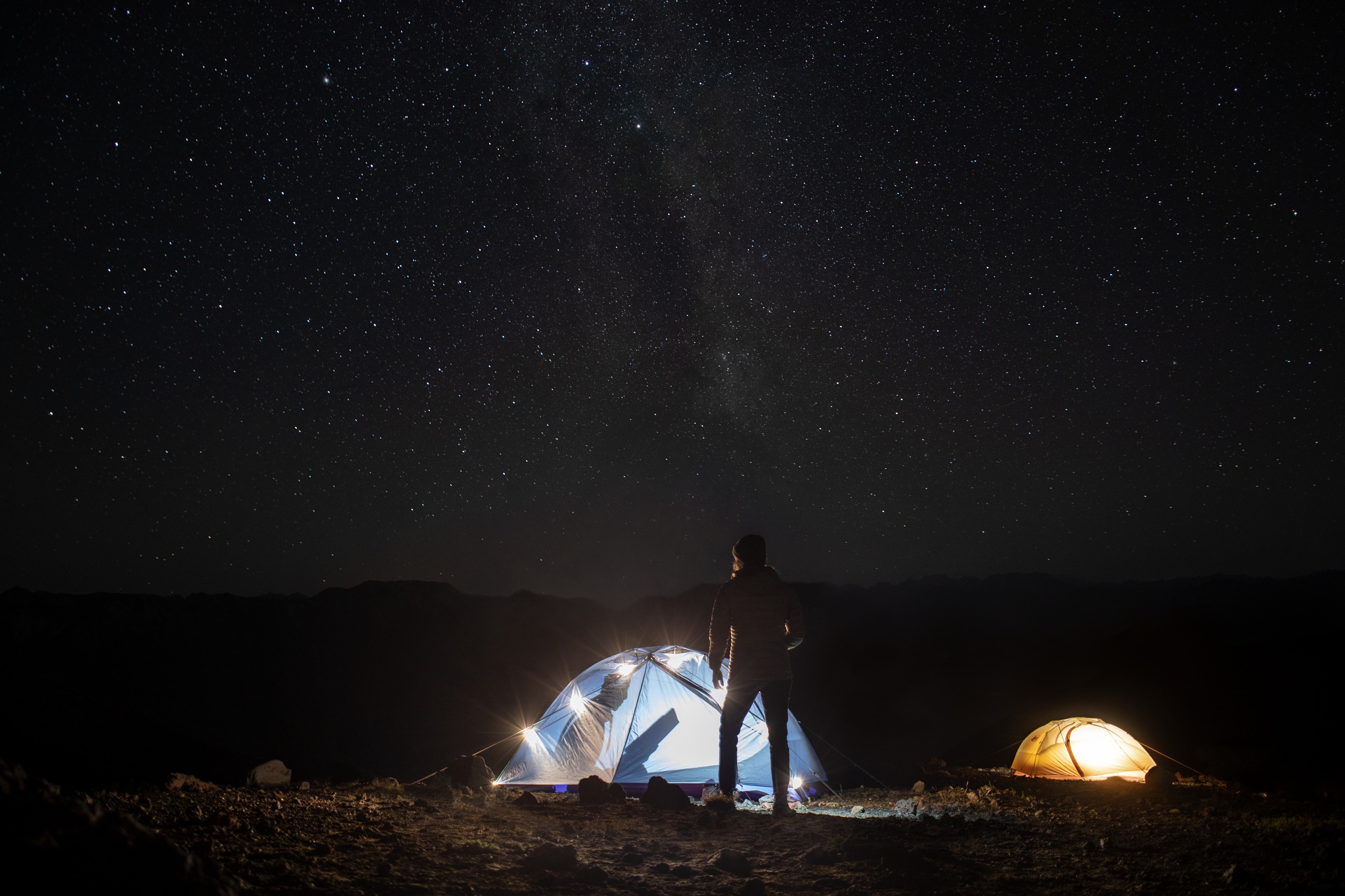 Two campers stargaze with only the glow of their tents