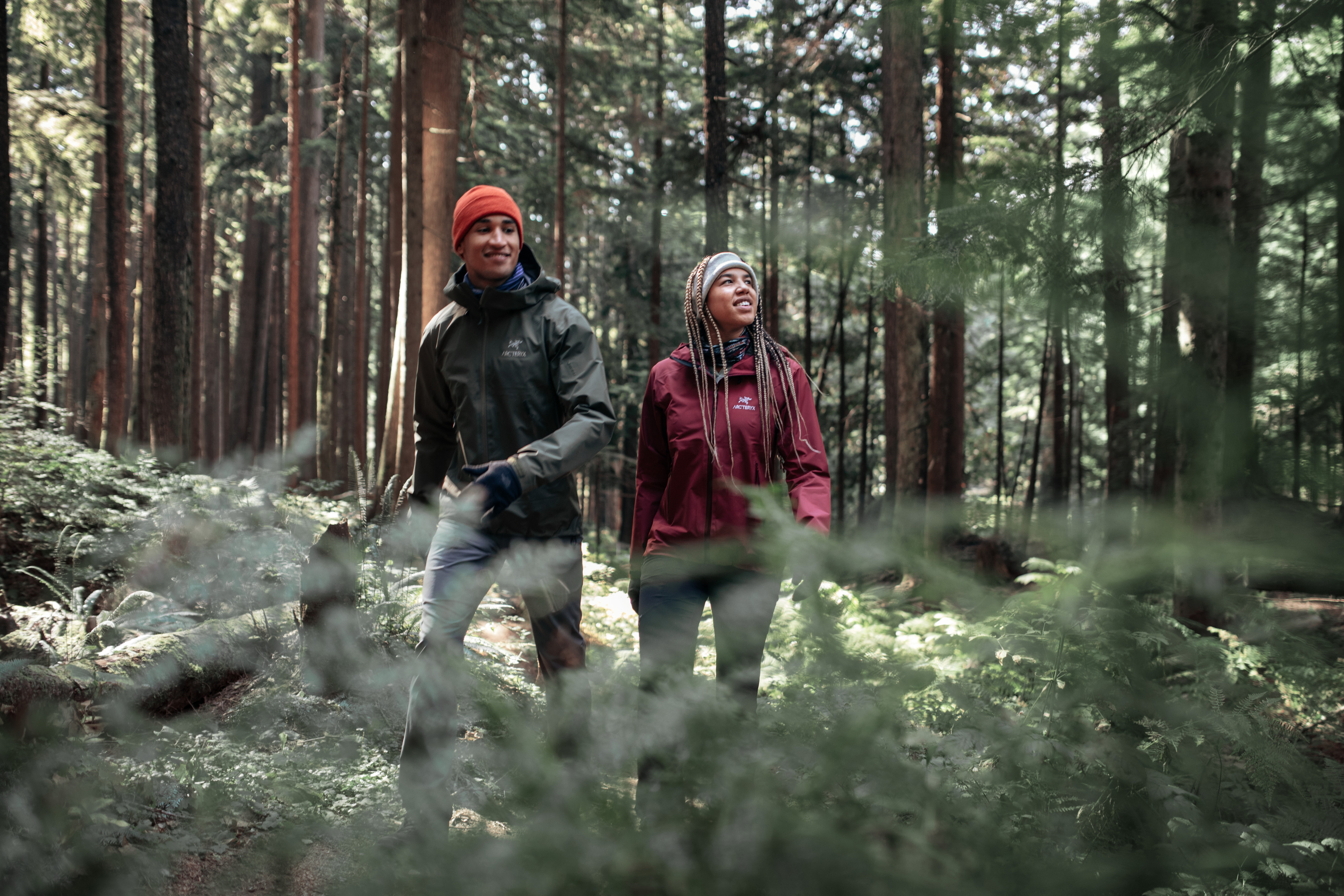 Two people wearing rain jackets hike through the woods.