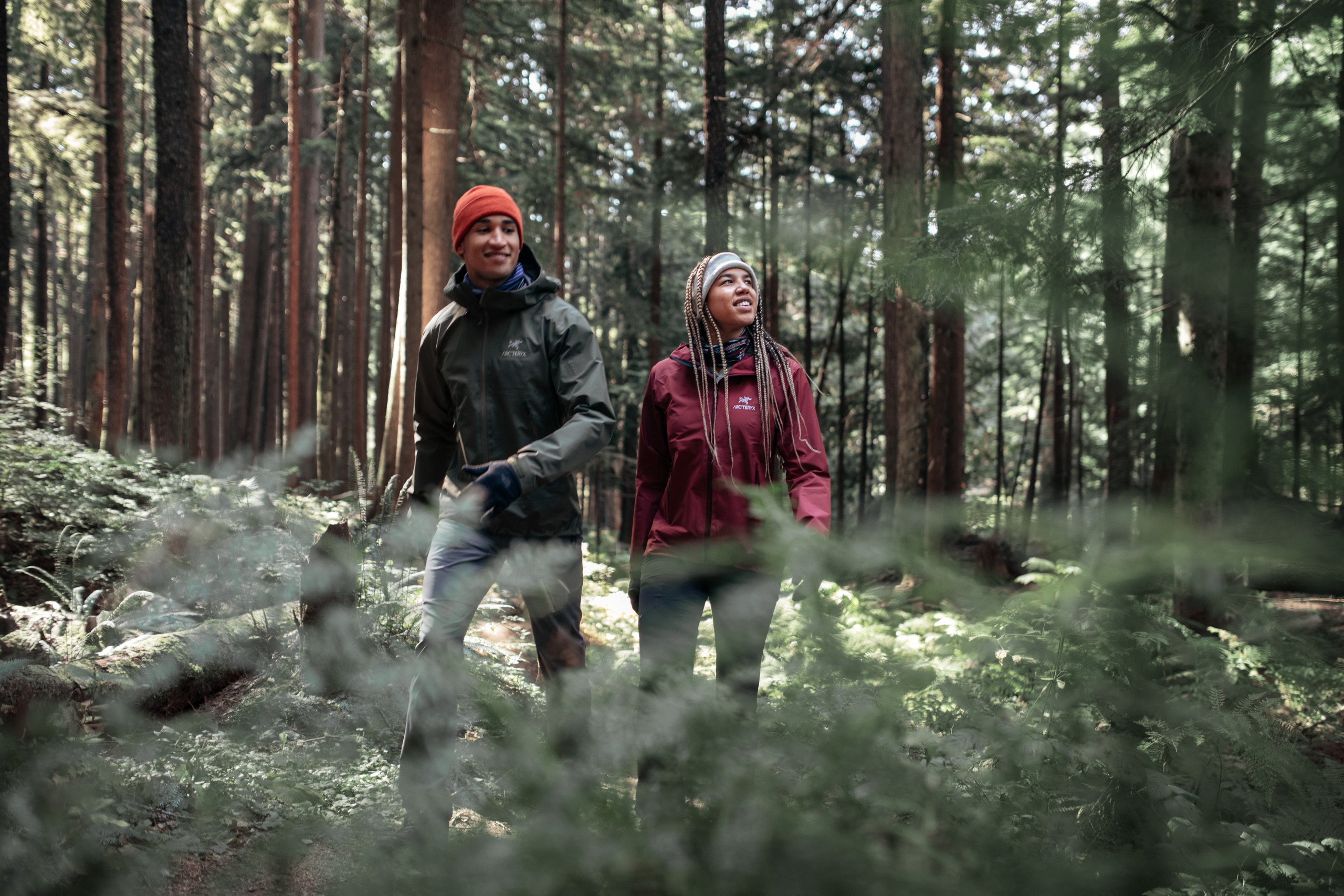 Two people wearing rain jackets hike through the woods.