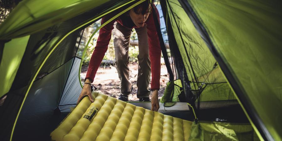 Picture of a person placing a sleeping pad inside a tent.