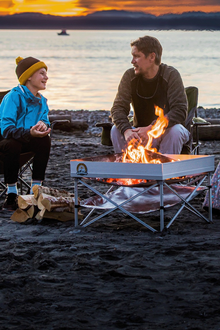Three people enjoying time by the fire at the beach at sunset.