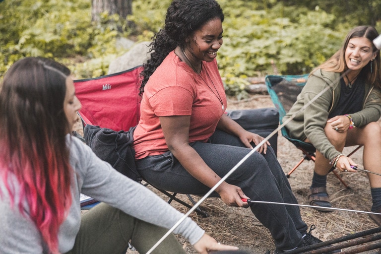 Three people sit around a campfire, smiling and talking