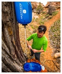A camper hangs a gravity filter from a tree