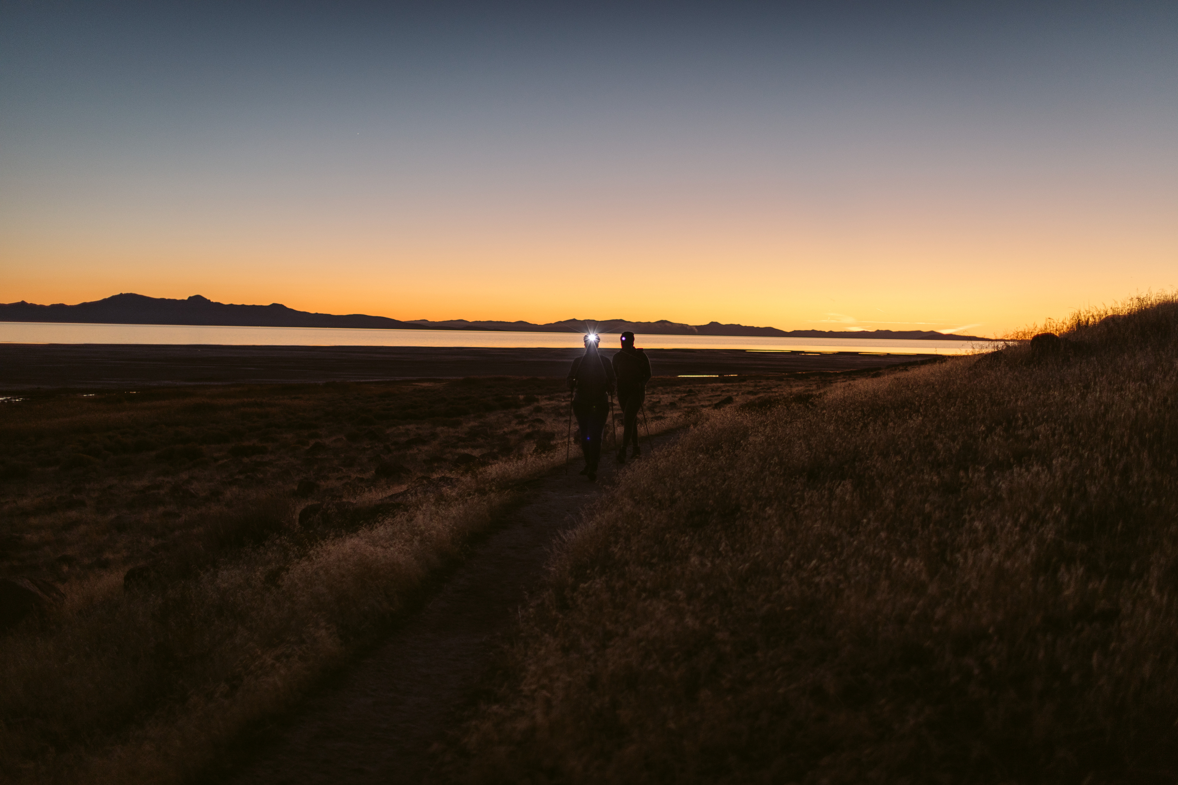 Two hikers at dawn with headlamps and trekking poles