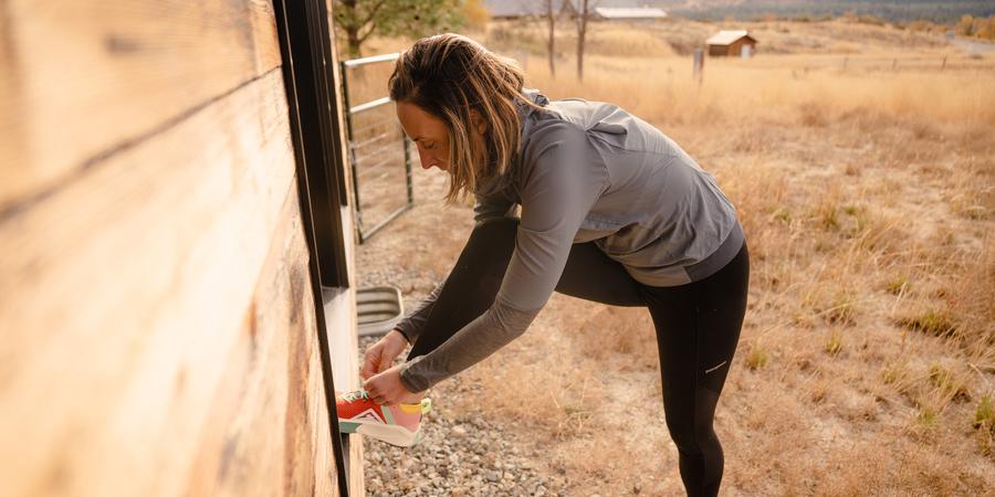 A runner puts her foot up against a window sill to tie her shoes.