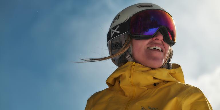 A person in snow goggles wearing a yellow jacket and white helmet looks off camera