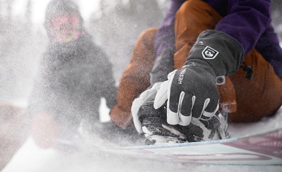 A person wearing gloves adjusts their shoe in snowy conditions
