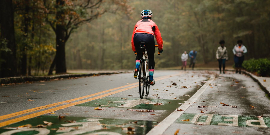 person biking on a wet road wearing bike pants and a rain jacket