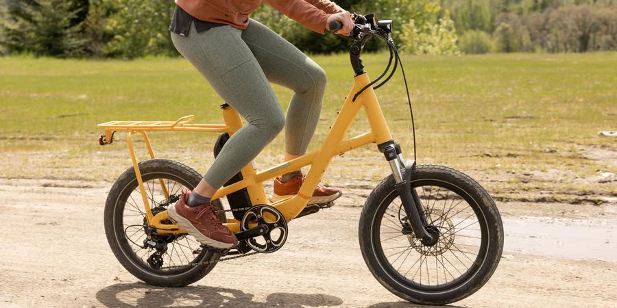 Person riding a yellow electric bike on a dirt path